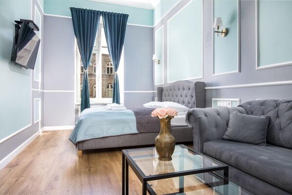 A modern hotel room with a bed, a gray sofa, a glass coffee table, and a vase of flowers.