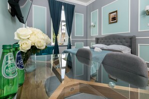 A hotel room with a bed, a chair, a table with a vase of flowers, and two bottles of beer.