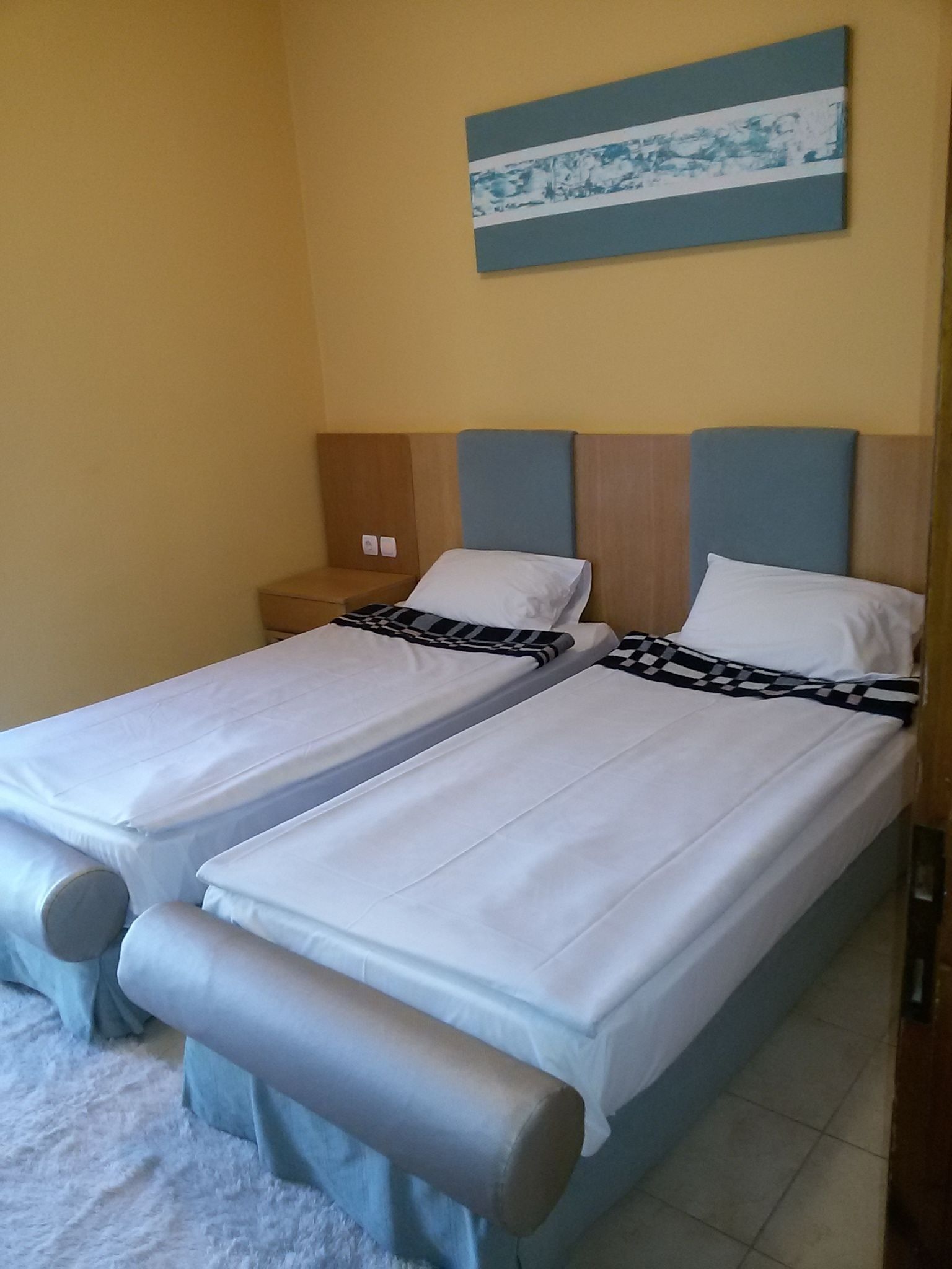 A double bed with a wooden headboard and a blue accent, two pillows, and a striped blanket.