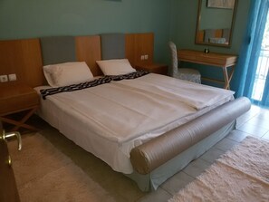 Siististi pedattu sänky, jossa on kuviollinen päiväpeite, puinen pääty ja yöpöytä, jossa on lamppu.