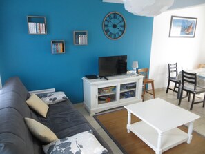 A living room with a blue wall, a white entertainment unit, a black TV, and a dining area with a table and chairs.