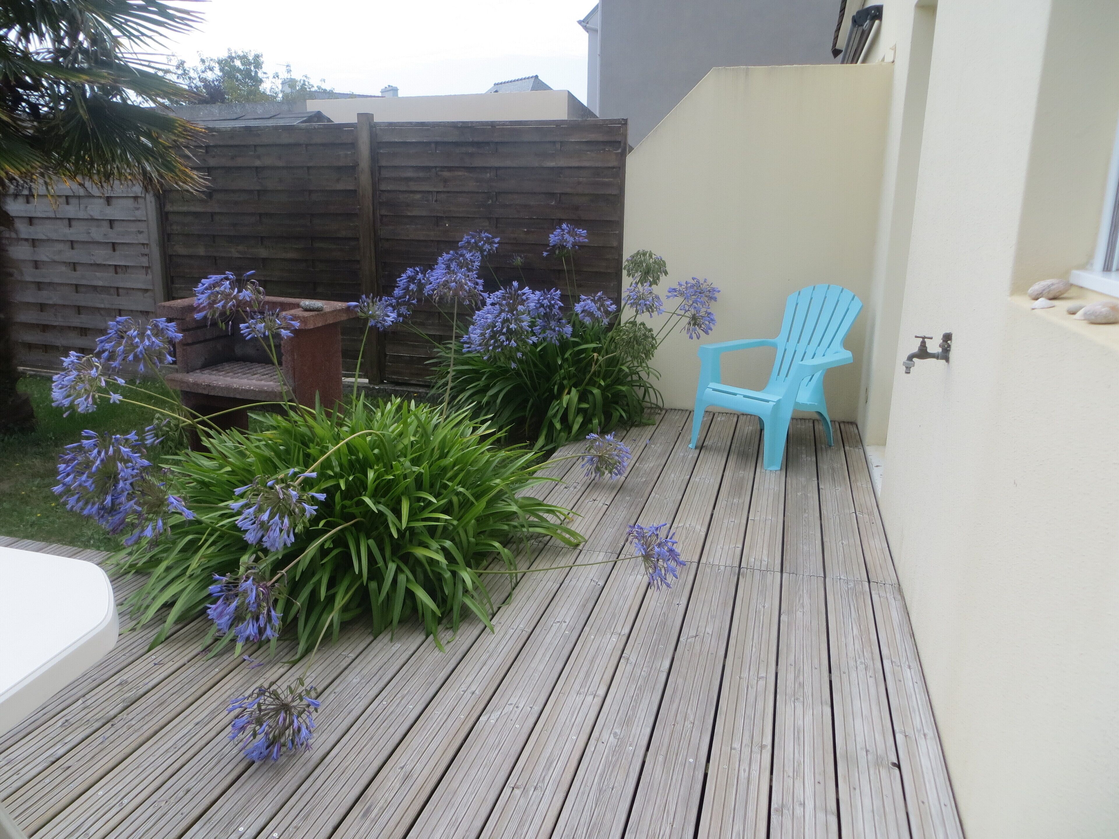 Une terrasse en bois avec une chaise bleue et des plantes en pot.