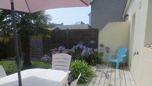 Een terras buiten met een houten terras, een witte tafel, twee stoelen en een blauwe stoel.