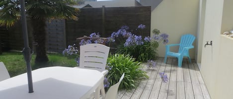 Um pátio externo com deck de madeira, uma mesa branca, duas cadeiras e uma cadeira azul.