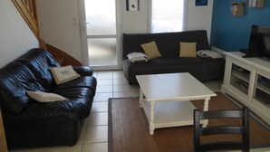 Een woonkamer met een zwarte leren bank, een witte salontafel, een zwarte fauteuil en een televisie op een kast.