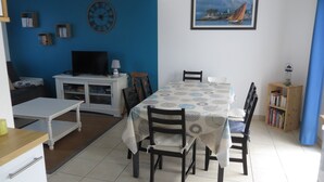 Een eethoek met een tafel voor vier personen, omringd door stoelen, een televisie en een boekenkast.