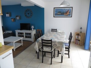 A dining area with a table set for four, surrounded by chairs, a television, and a bookshelf.