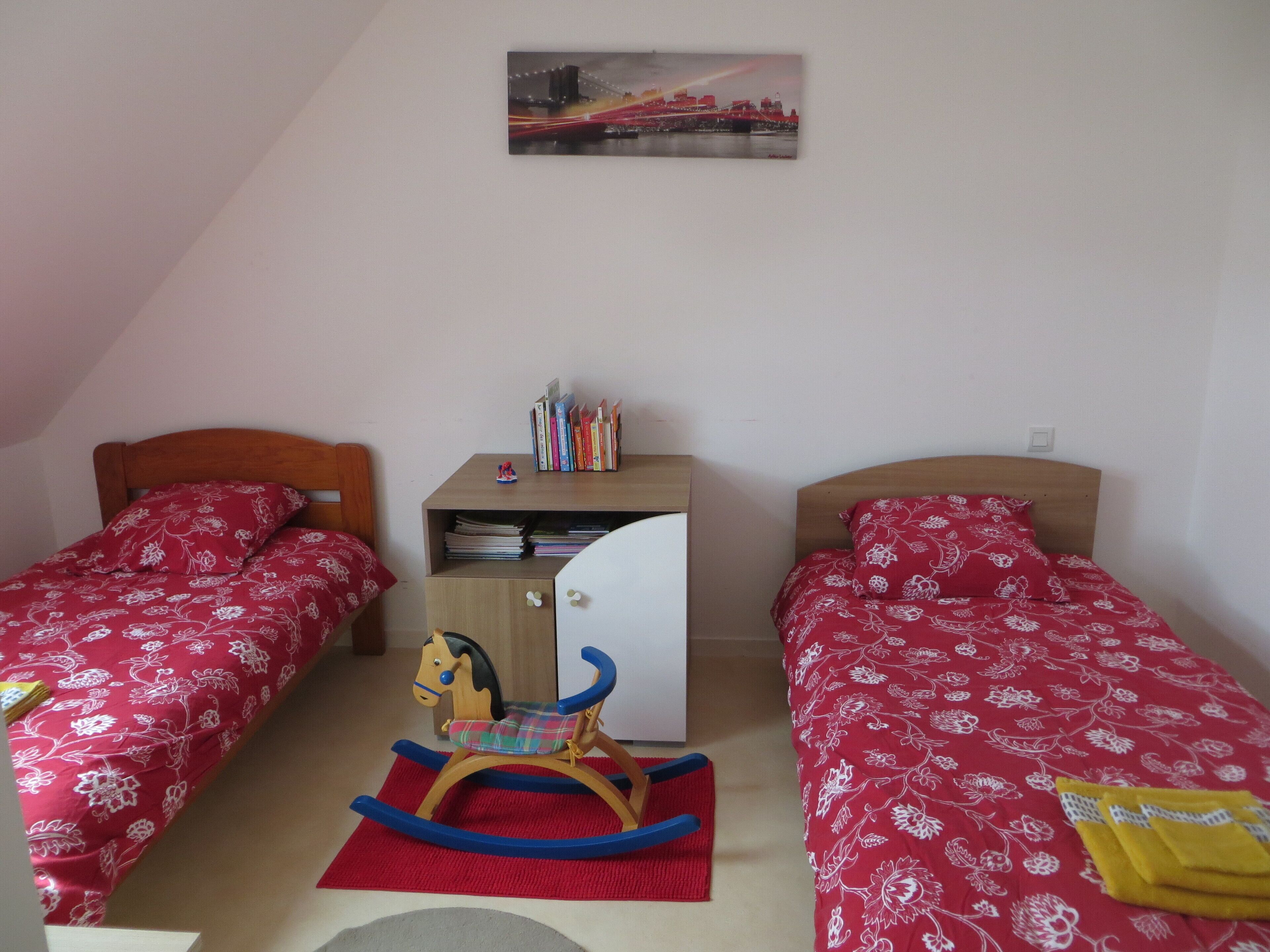 Ein Schlafzimmer mit zwei Einzelbetten, einem Schaukelpferd, einem Schreibtisch mit Büchern und einem Bild an der Wand.