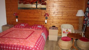 A wooden-paneled room with a bed, two nightstands, a chair, a small table, and a lamp. - BEAUTIFUL VIEW APARTMENT 50 M2, 2 Bedrooms, 1 shower room, 4 people. (La Bresse)