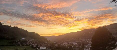 A panoramic view of a town with buildings and greenery, under a sunset sky.