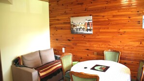 A room with a wooden wall, a round table with a white tablecloth, and a sofa with a blanket. - BEAUTIFUL VIEW APARTMENT 50 M2, 2 Bedrooms, 1 shower room, 4 people. (La Bresse)