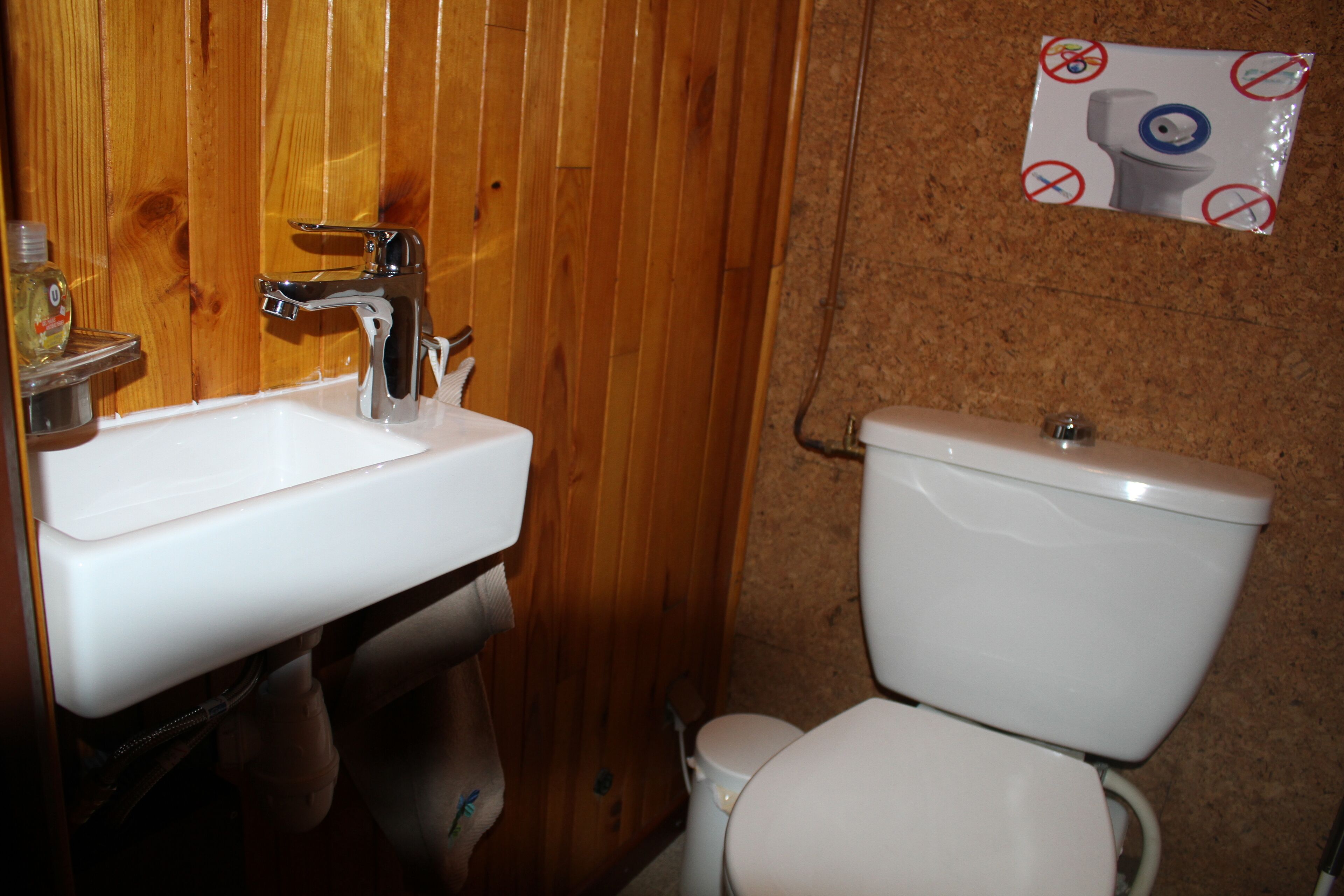 Pieni kylpyhuone, jossa on puinen seinä, valkoinen pesuallas ja wc-istuin.