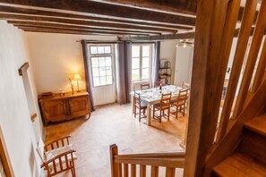 Ein Essbereich mit Holztisch, gedeckt für vier Personen, einer Holzkommode und einem Fenster mit Vorhängen.