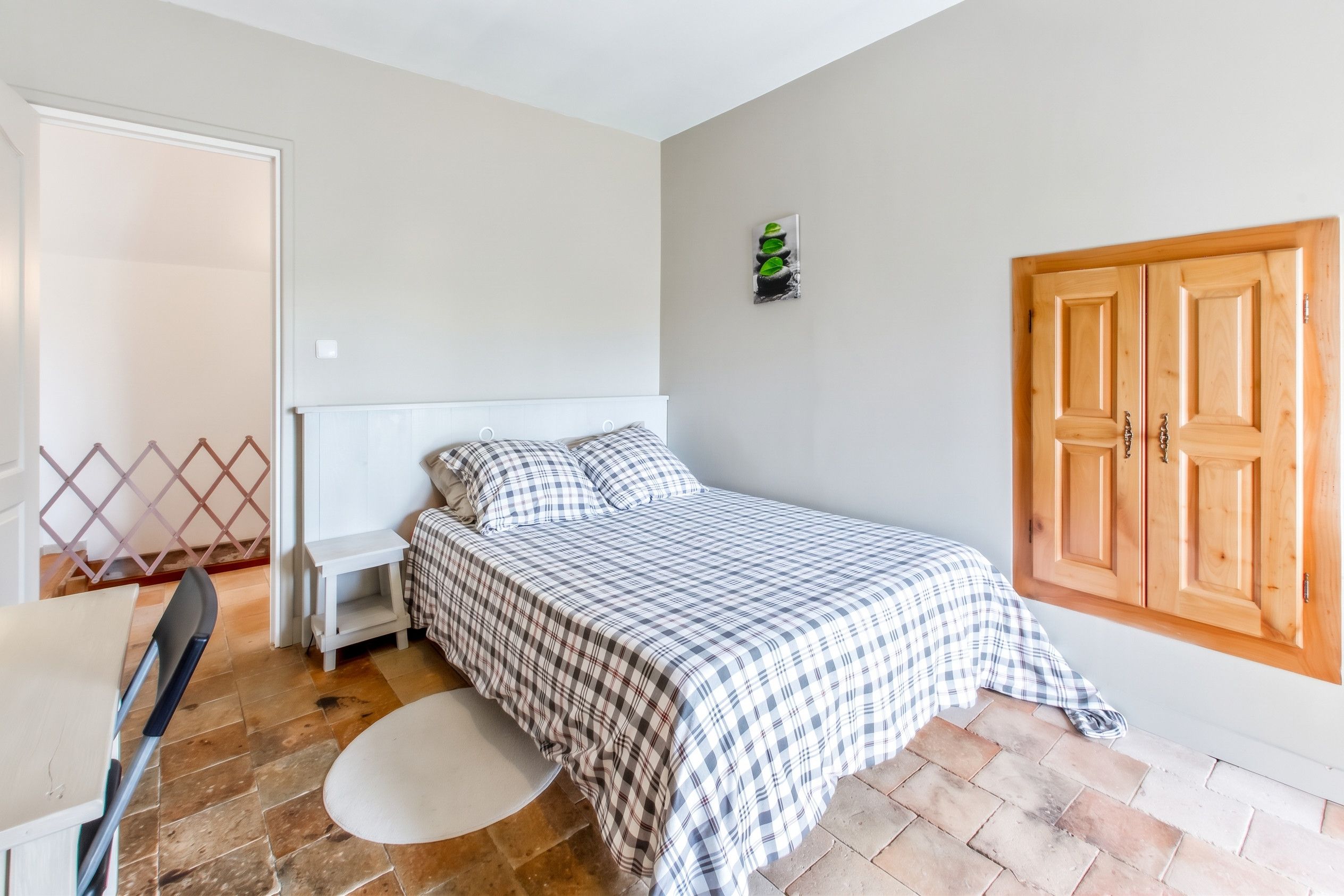 Une chambre à coucher avec un lit, une petite table de chevet, une lampe fixée au mur, une porte en bois et une fenêtre.