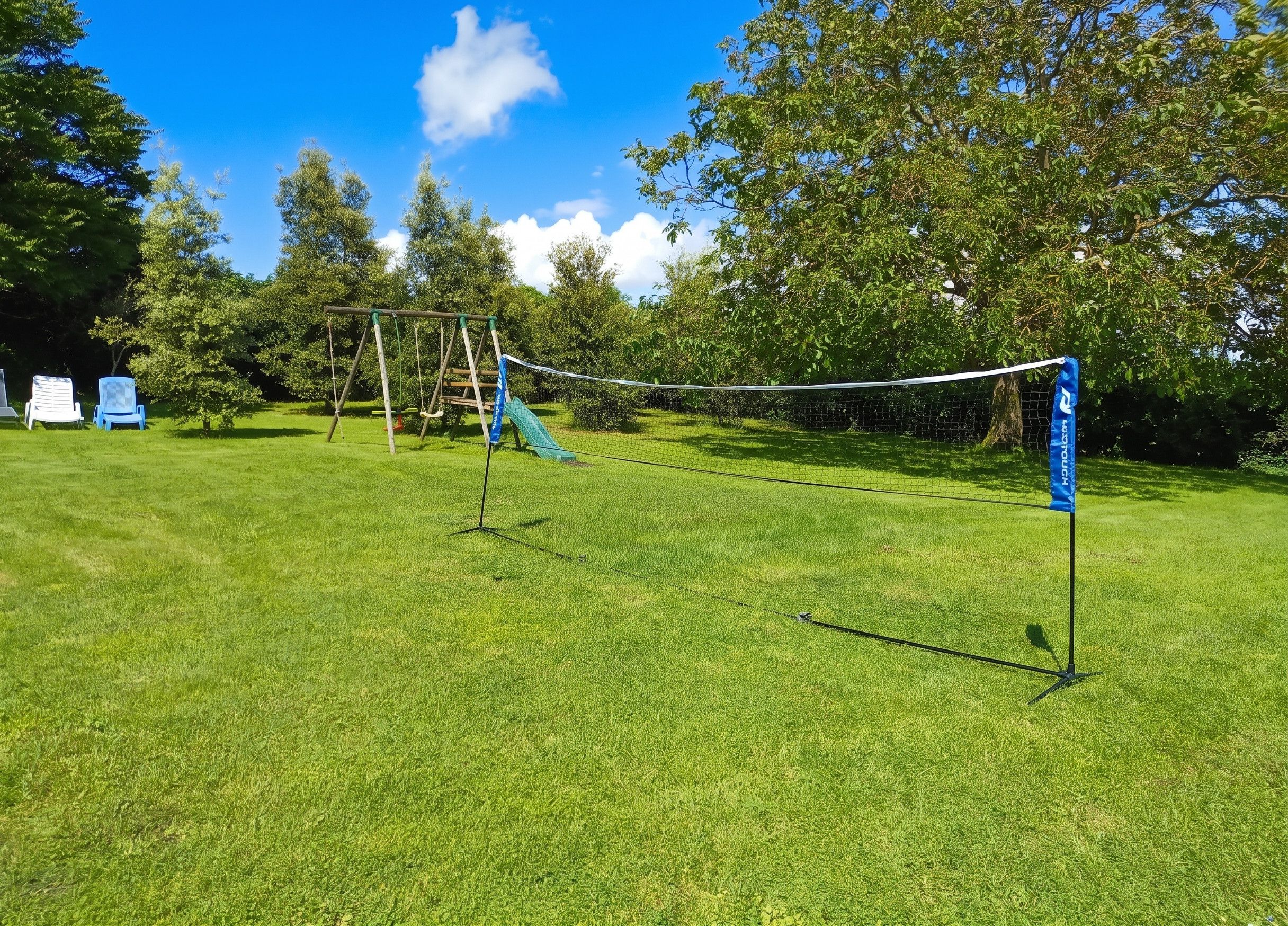 Ein grasbewachsenes Freigelände mit Volleyballnetz, Schaukeln und einer blauen Flagge.