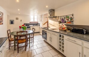 A modern kitchen with white cabinetry, a dining table with chairs, and a built-in oven. - Homerez - House in Assay (Assay)