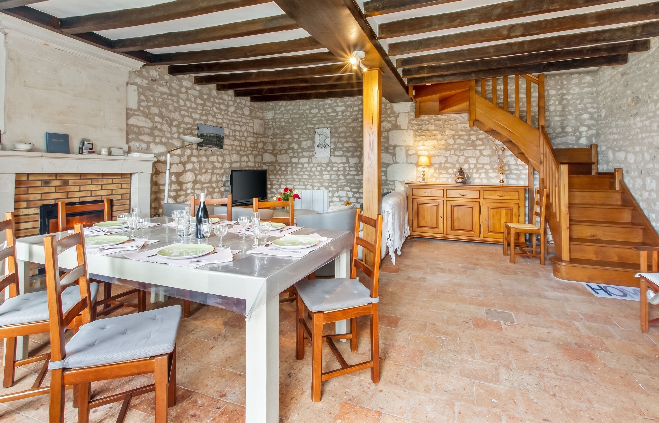 Un comedor con pared de piedra, vigas de madera en el techo y una escalera que lleva a un nivel superior.