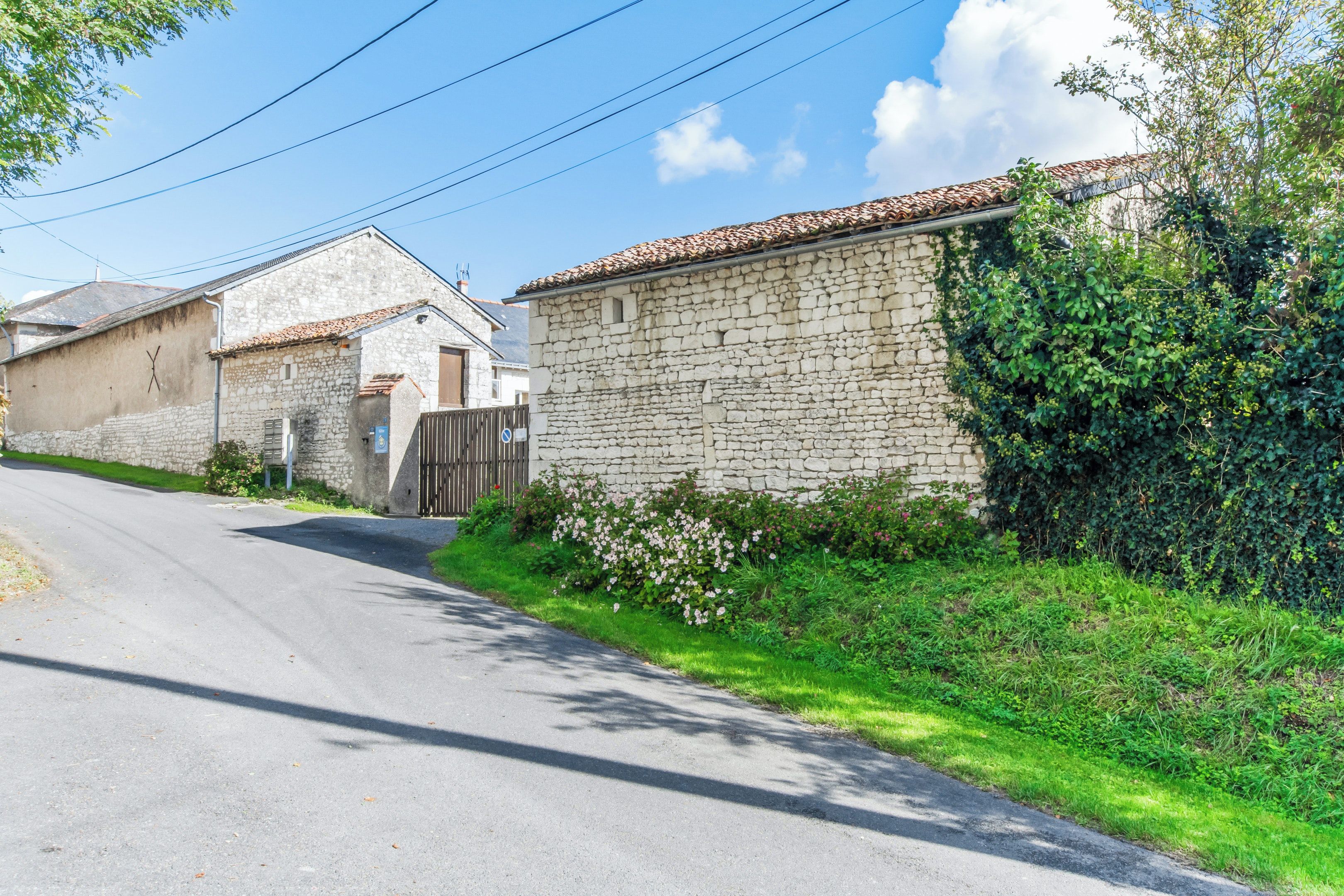 A narrow street with stone buildings, a gated entrance, and lush greenery.