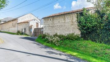 A narrow street with stone buildings, a gated entrance, and lush greenery.