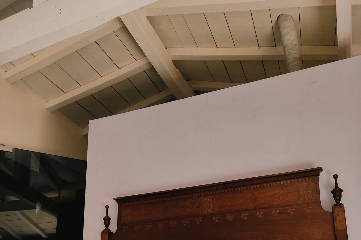 A neatly made bed with a wooden headboard, white and maroon pillows, and a white bedspread.