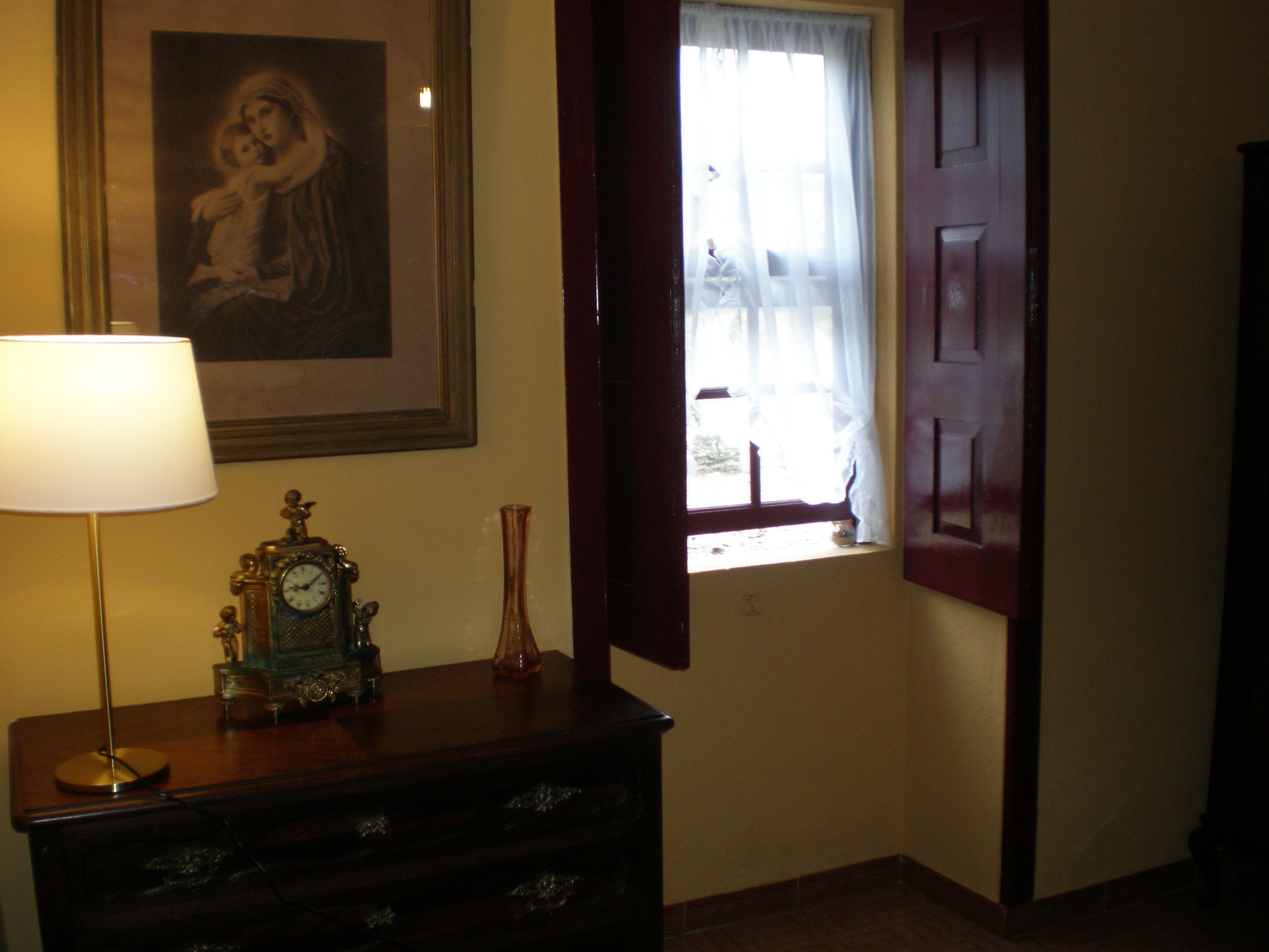 Une pièce avec une commode en bois, un tableau encadré au mur, une fenêtre avec des rideaux et une porte.