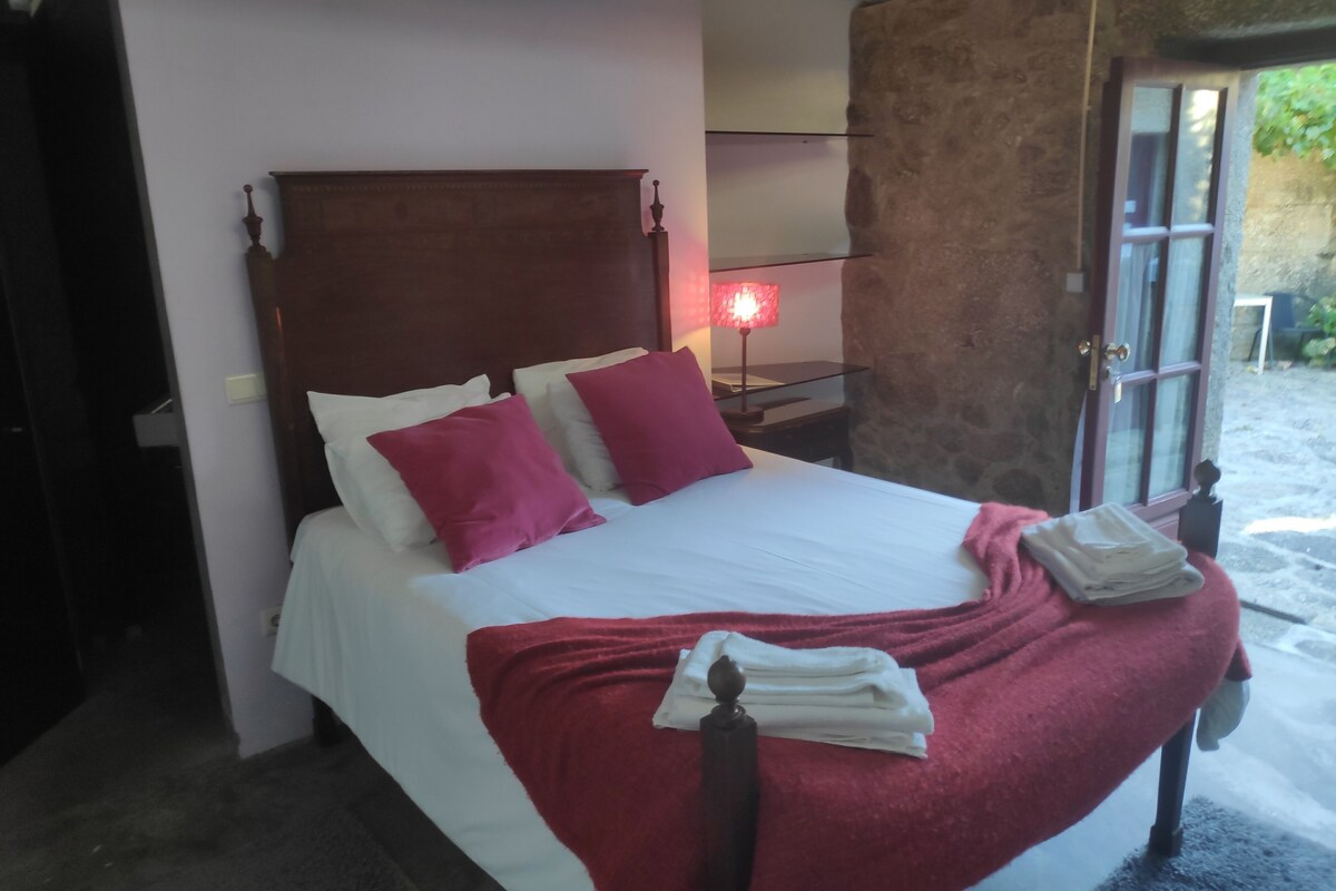 A bed with a wooden headboard, white bedding, and red pillows. There is a bedside lamp, a window with a view, and a stack of folded towels on the bed.