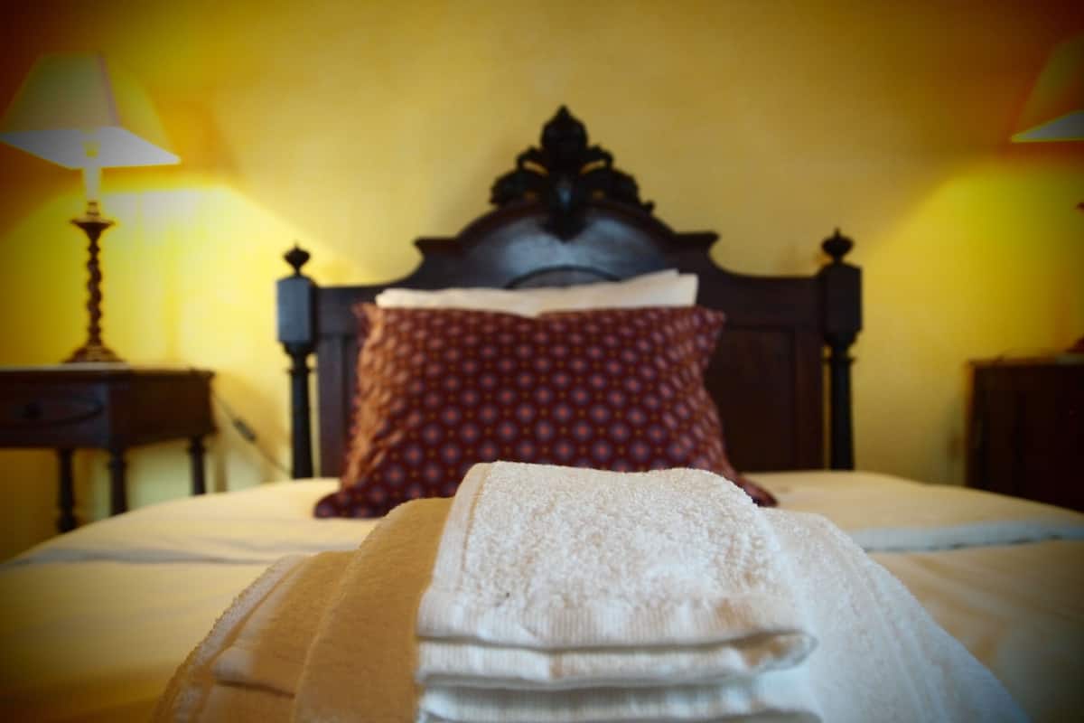A neatly made bed with a folded towel in the foreground, a wooden headboard, and a patterned pillow.