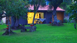 Uma casa com telhado de telhas vermelhas, área de jantar com mesa e cadeiras, e um jardim com um banco e um cacto.