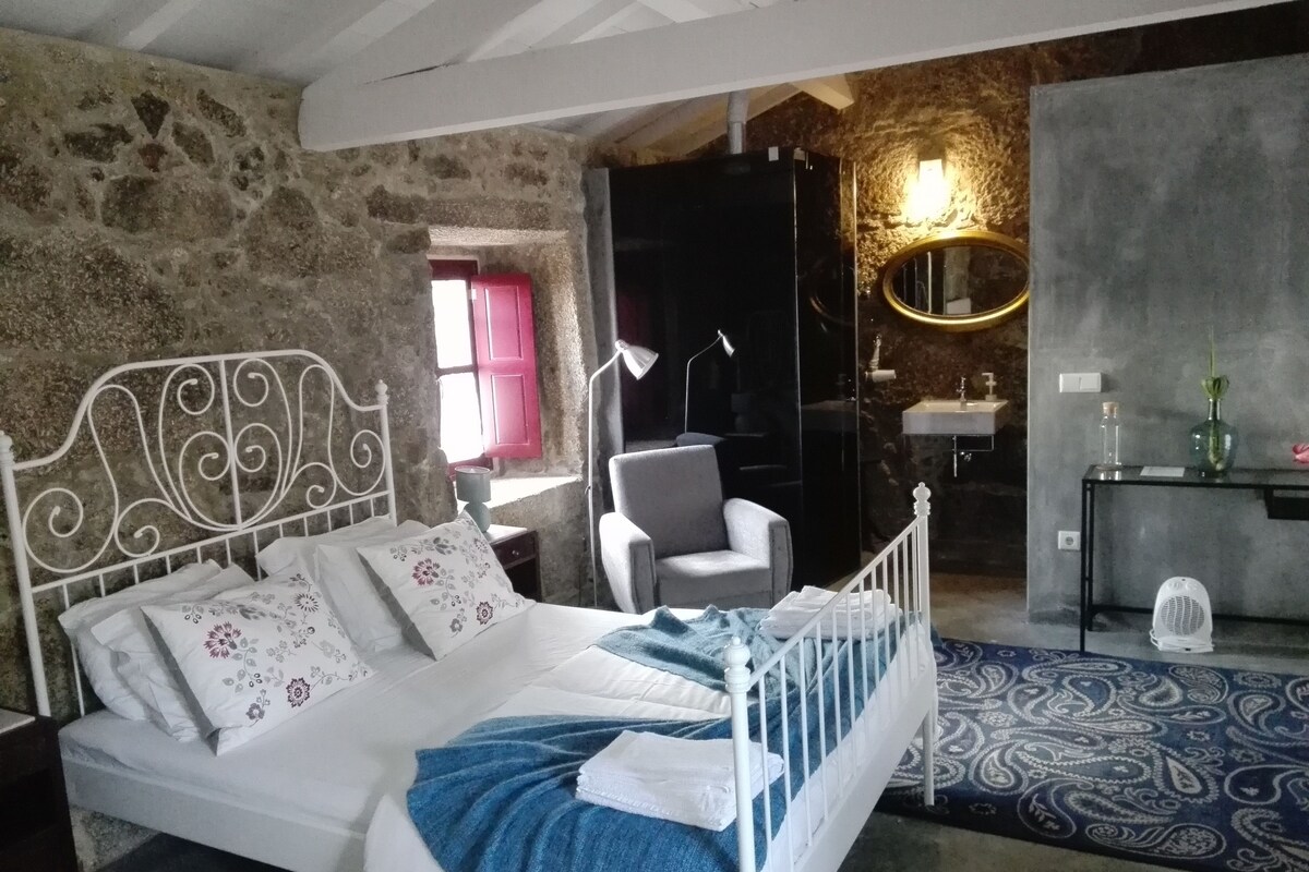 A bedroom with a bed, a chair, a desk, a mirror, and a bathroom.