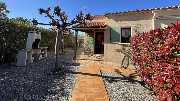 A house with a tiled roof, a covered porch, and a gravel driveway.