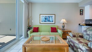 A living room with a green sofa, a glass coffee table, a patterned armchair, a lamp, and a framed picture on the wall. - LIGHTHOUSE! One Bedroom XTRA BATH! Low Floor Beach Front (Gulf Shores)