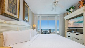 A hotel room with a large bed, a television, and a balcony with a view of the beach.