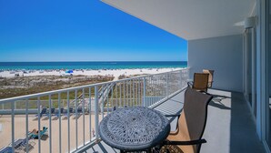 A balcony with a view of a beach, a round table, and two chairs.
