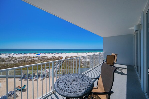 Ein Balkon mit Blick auf einen Strand, einem runden Tisch und zwei Stühlen.