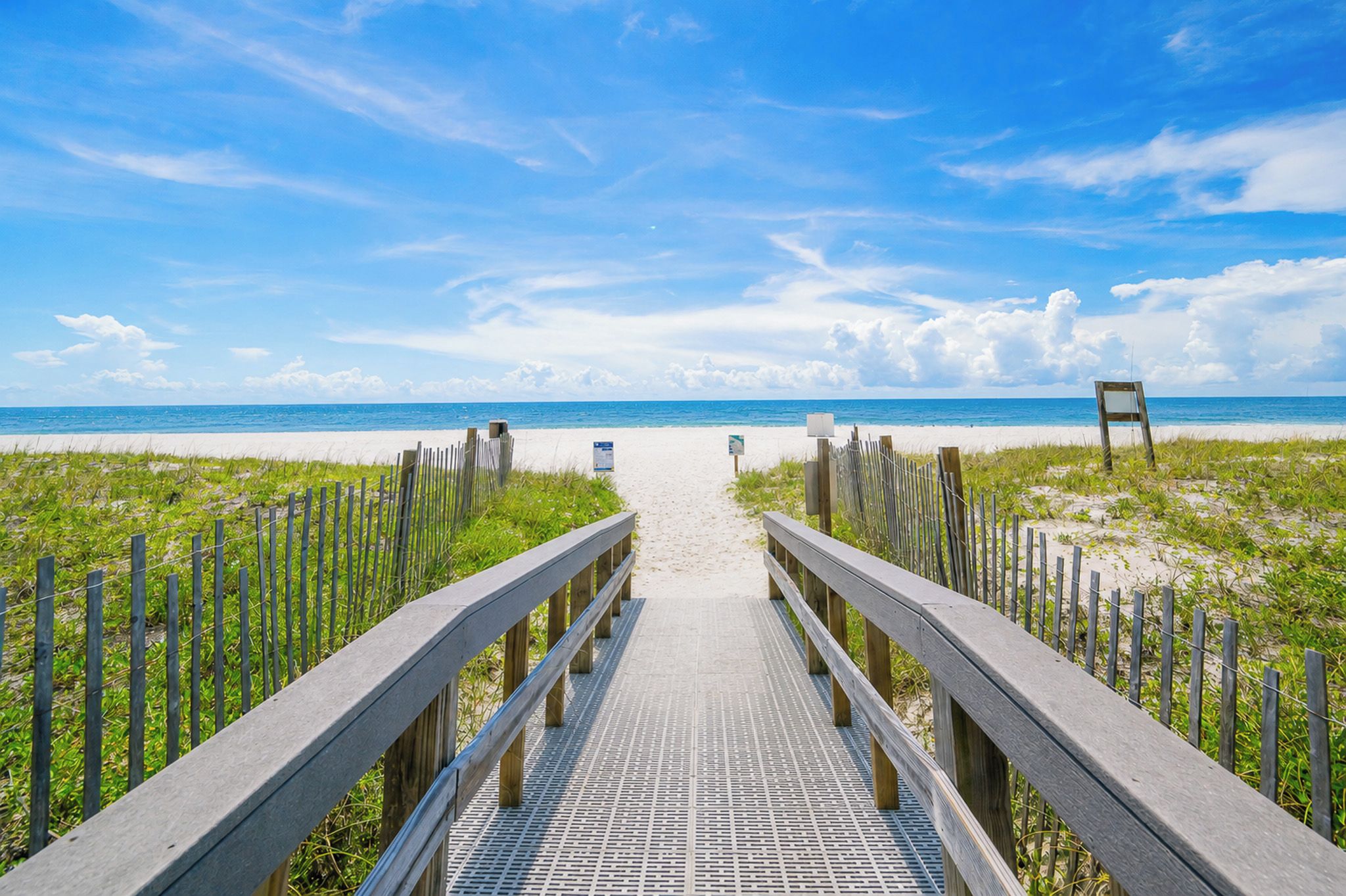 A wooden boardwalk leading to a beach with a clear sky.