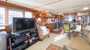 A spacious living area with a large flat-screen TV, a cozy armchair, a dining table with chairs, and a kitchen area with a refrigerator and microwave. - NOT YOUR TYPICAL HOUSEBOAT: 60 FEET OF FUN! (Sanford)