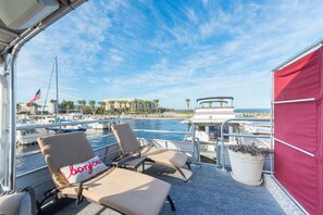 A boat deck with lounge chairs, a potted plant, and a view of the marina and beach.
