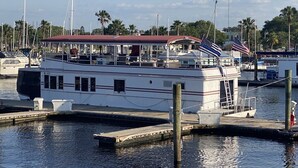 A large boat docked at a marina with a covered deck area and an American flag. - NOT YOUR TYPICAL HOUSEBOAT: 60 FEET OF FUN! (Sanford)