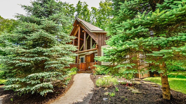 A log cabin with a wooden deck and a covered porch, surrounded by dense evergreen trees. - Deep Creek Gem w/ Indoor Hot Tub (OAKLAND)