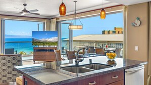 Una cocina con una isla grande, un comedor con sillas y una mesa, y vistas al océano.