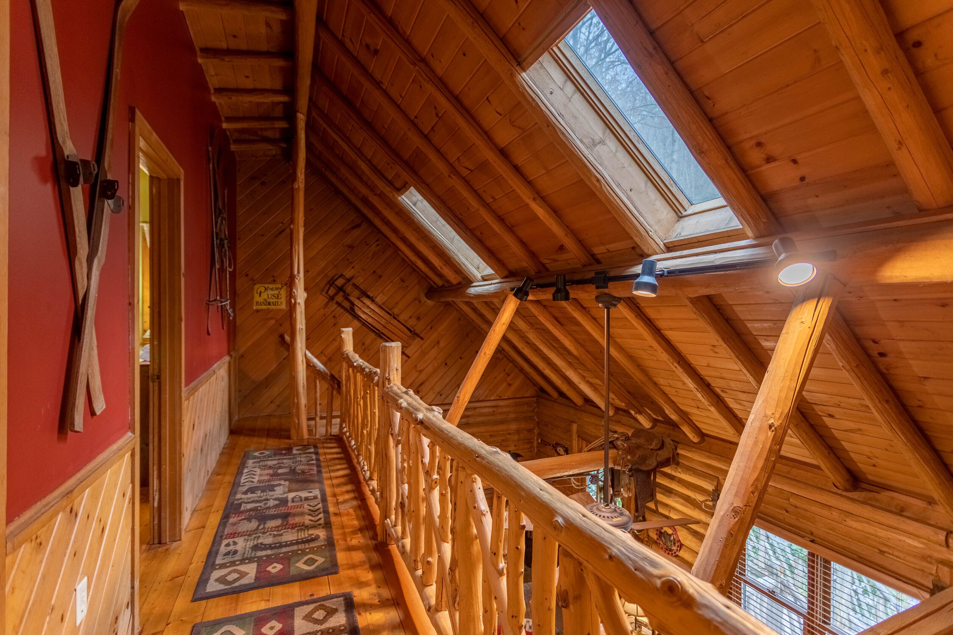 Ein Dachzimmer aus Holz mit Dachfenstern, einer Holzleiter und einem gemusterten Teppich.