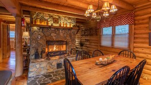 A cozy log cabin interior with a stone fireplace, wooden dining table, and black chairs. - Draggin Fly- Romantic Getaway! River Frontage - Hot Tub - Firepit (Vilas)