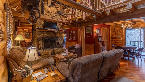 A log cabin interior with a stone fireplace, leather furniture, and a wooden staircase. - Draggin Fly- Romantic Getaway! River Frontage - Hot Tub - Firepit (Vilas)