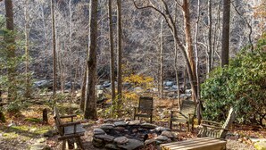 A forested area with a fire pit, benches, and a wooden table. - Draggin Fly- Romantic Getaway! River Frontage - Hot Tub - Firepit (Vilas)