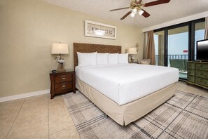 A bedroom with a large bed, two bedside tables, a ceiling fan, a framed picture on the wall, and a view of the outdoors through a sliding door.
