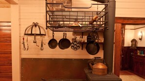 Une cuisine traditionnelle avec un poêle à bois, des casseroles suspendues et un porte-ustensiles.