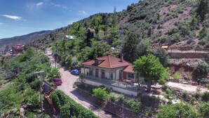 Une maison avec un toit recouvert de tuiles rouges, entourée d’une végétation luxuriante et de collines.