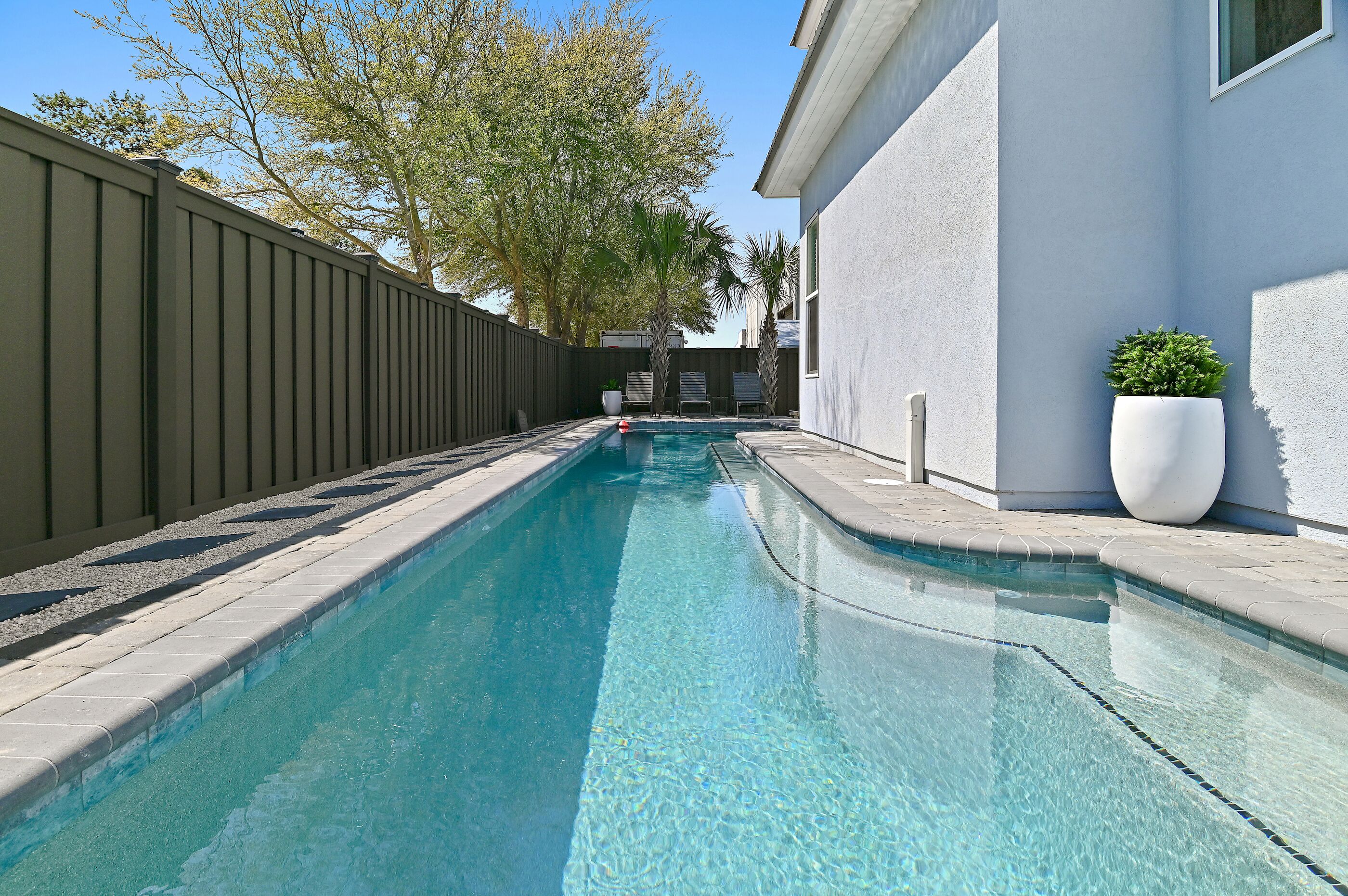Ein Schwimmbecken mit Holzzaun, weißer Wand und einem Blumentopf.