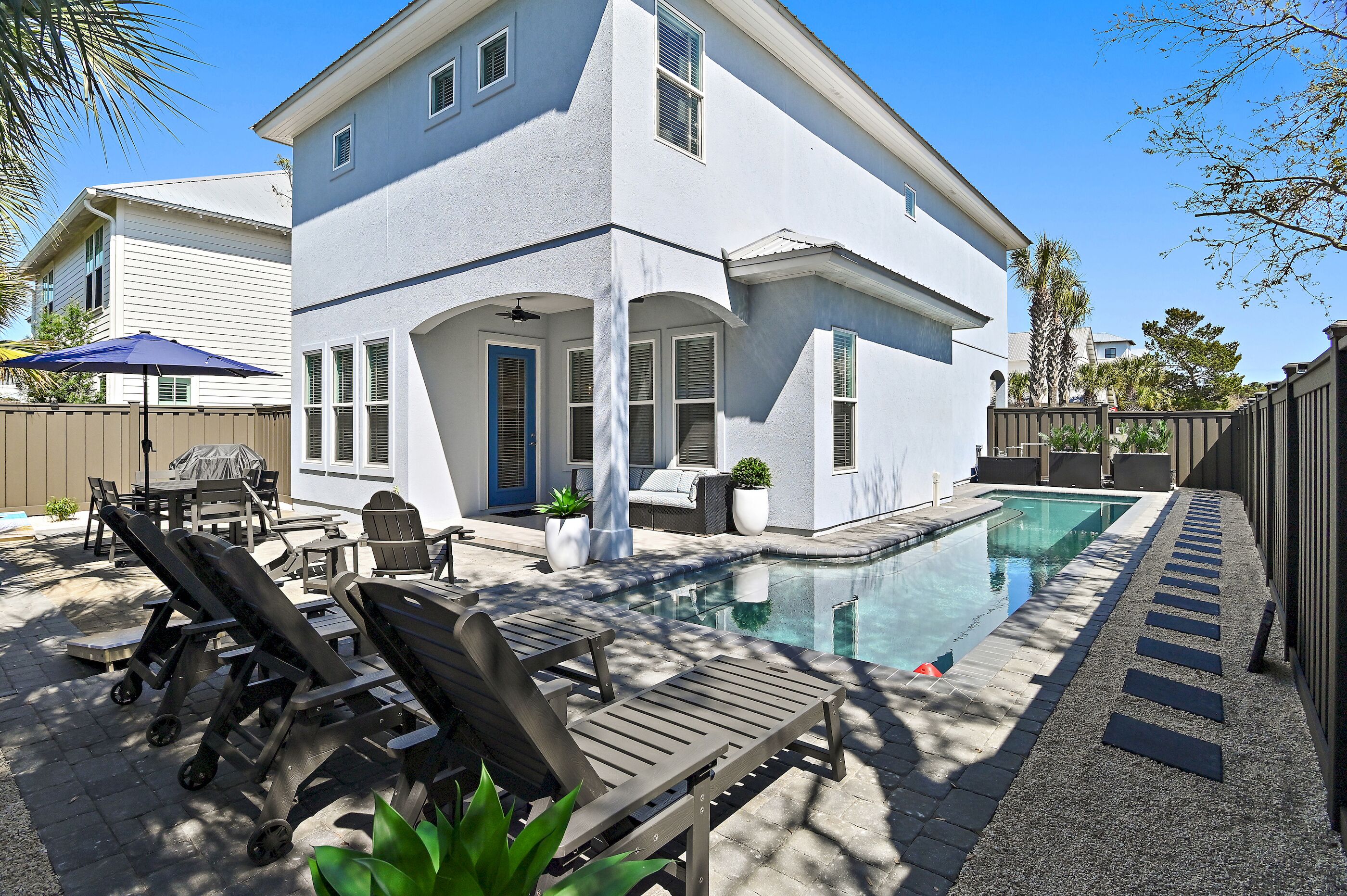 A two-story house with a swimming pool, outdoor furniture, and a fenced backyard.