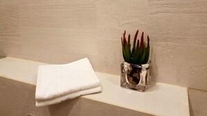 A bathroom with a white towel on a shelf and a glass vase with a plant. - Royal Apartment Tel Aviv (Tel Aviv)